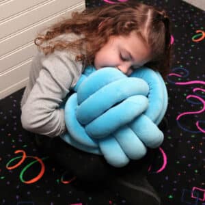 A girl holding a blue cuddle ball sensory pillow.